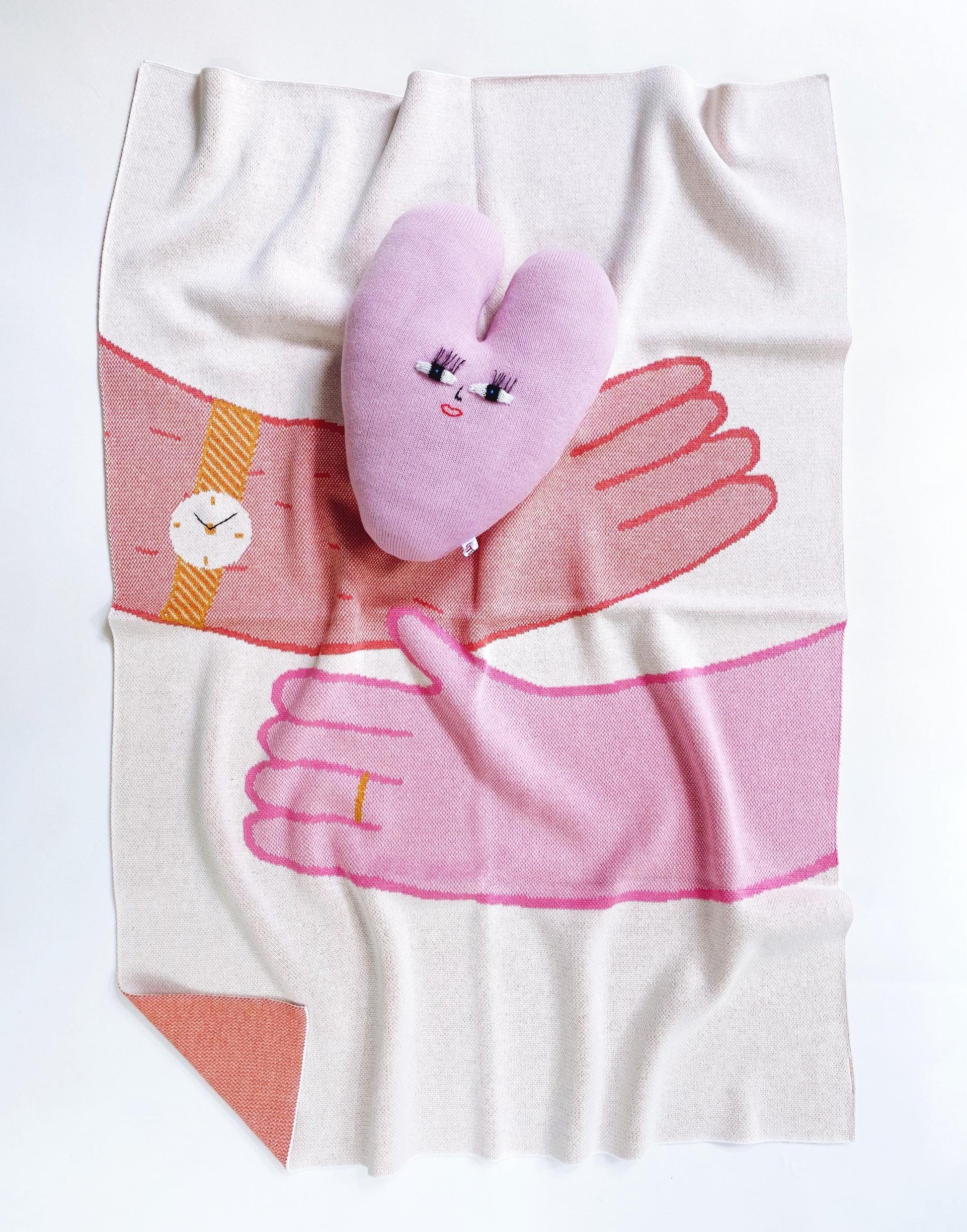 Blanket with a design of hands hugging holding a heart shaped pillow with a face on it 