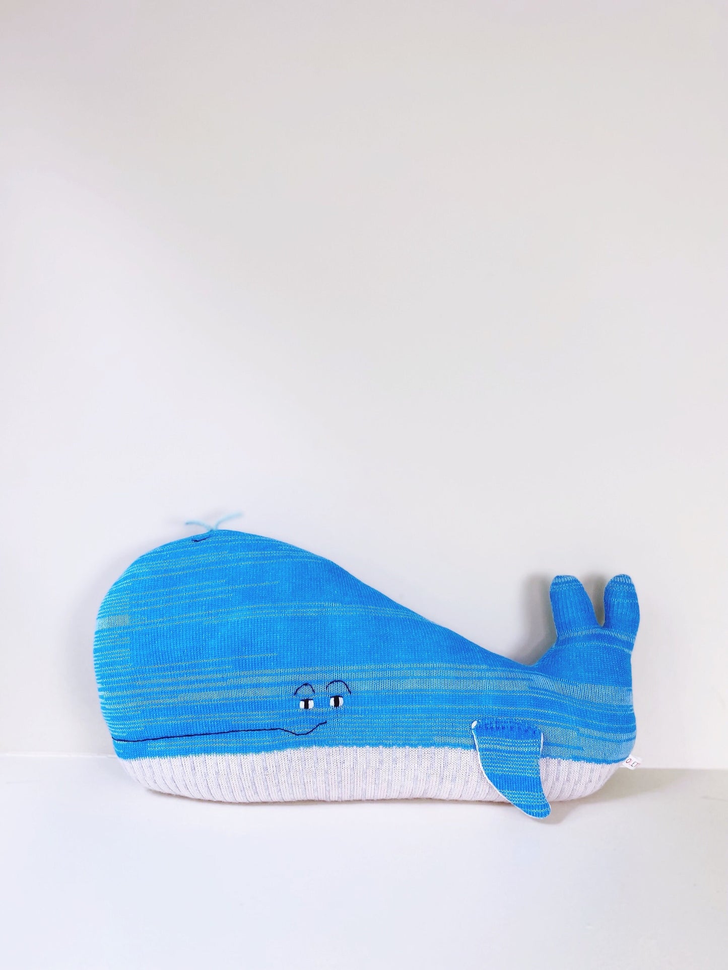 Blue knitted whale-shaped pillow plush on a white background