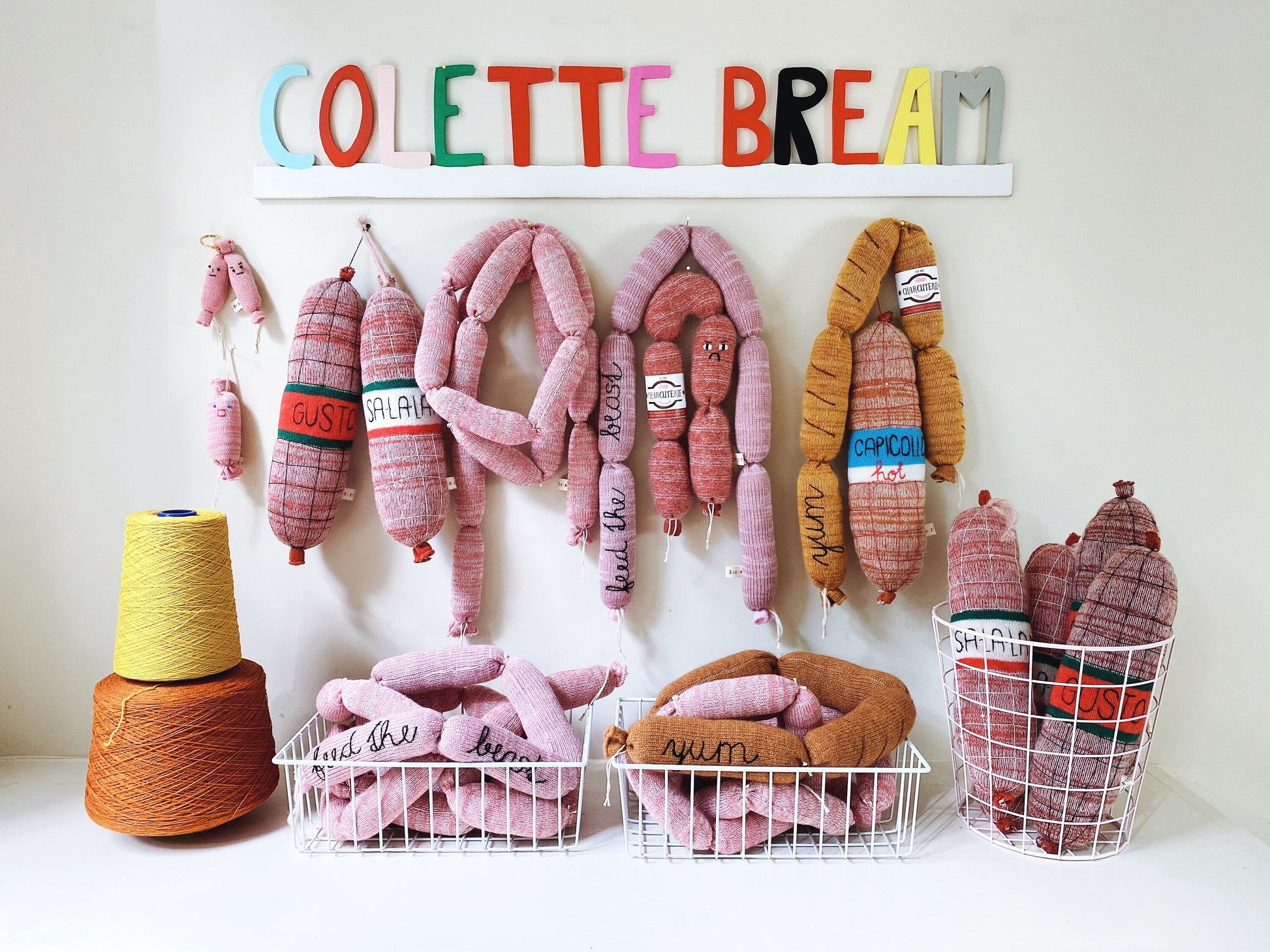 Decorative wall with knitted plush sausage links and salami and text 'COLETTE BREAM' on a white background