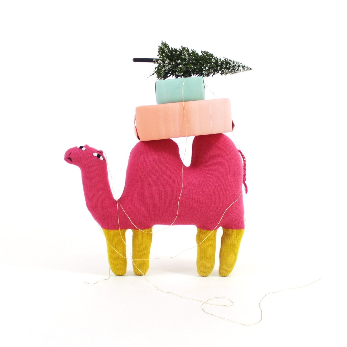 Pink knitted lambswool camel plush toy with a pink box and green miniature christmas tree on its back against a white background