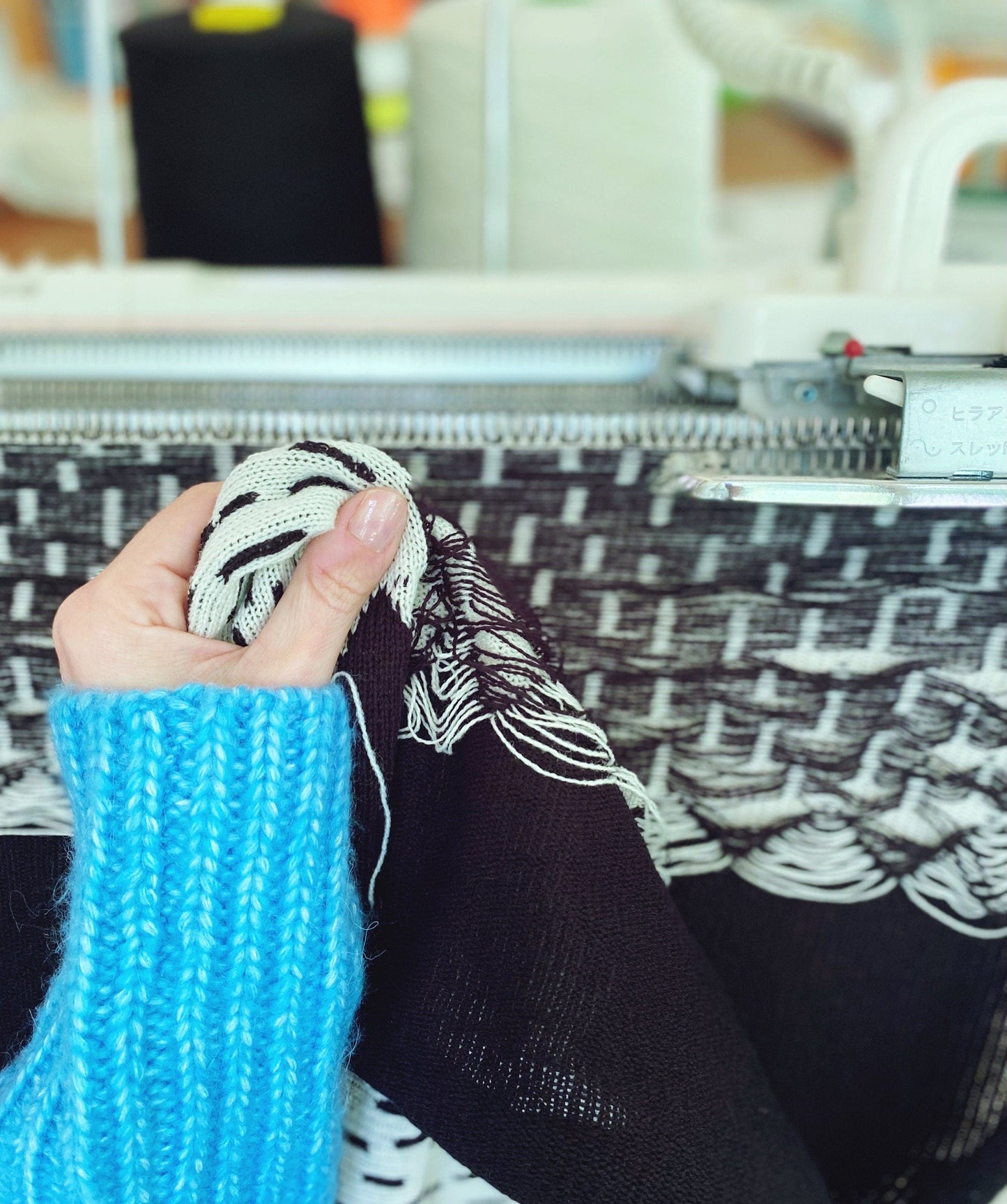 Person knitting with a patterned yarn and blue sleeves in a blurred indoor setting