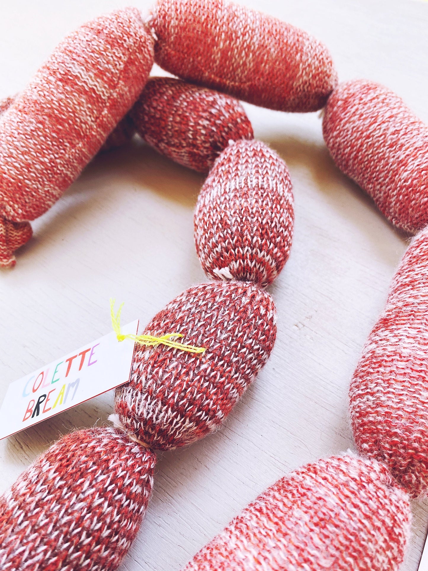 Lambswool knitted sausages on a light wooden surface with a colorful label