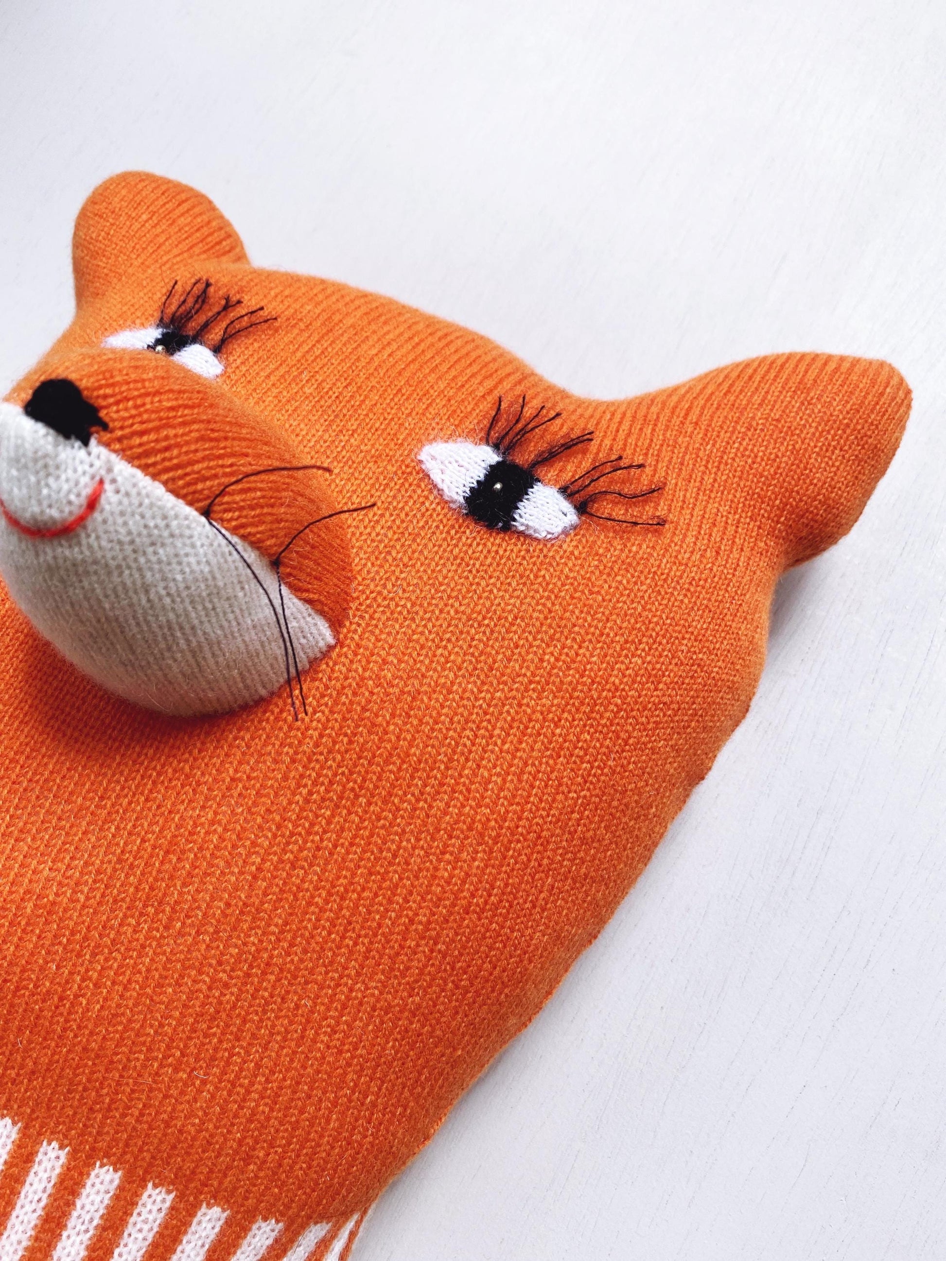 Orange fox-shaped knitted plush toy on a white background