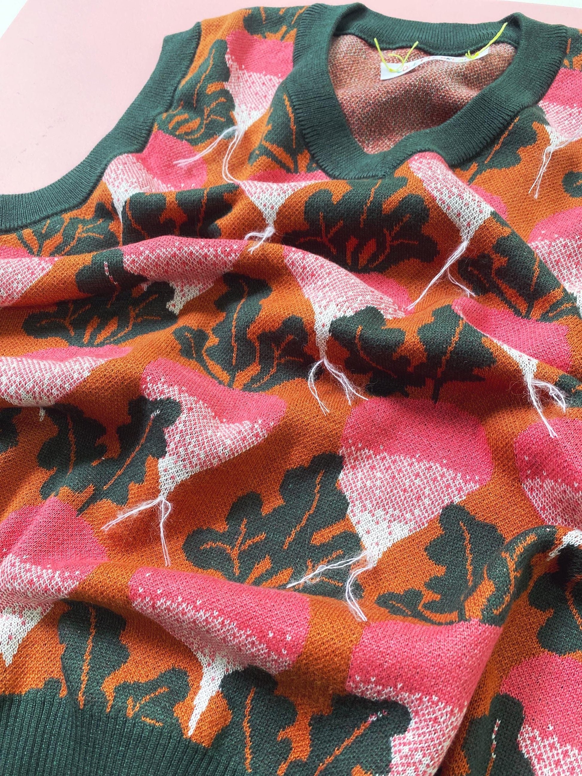 Close-up of a colorful knitted sweater vest with pink, orange, and green radish and beets patterns on a pink background.
