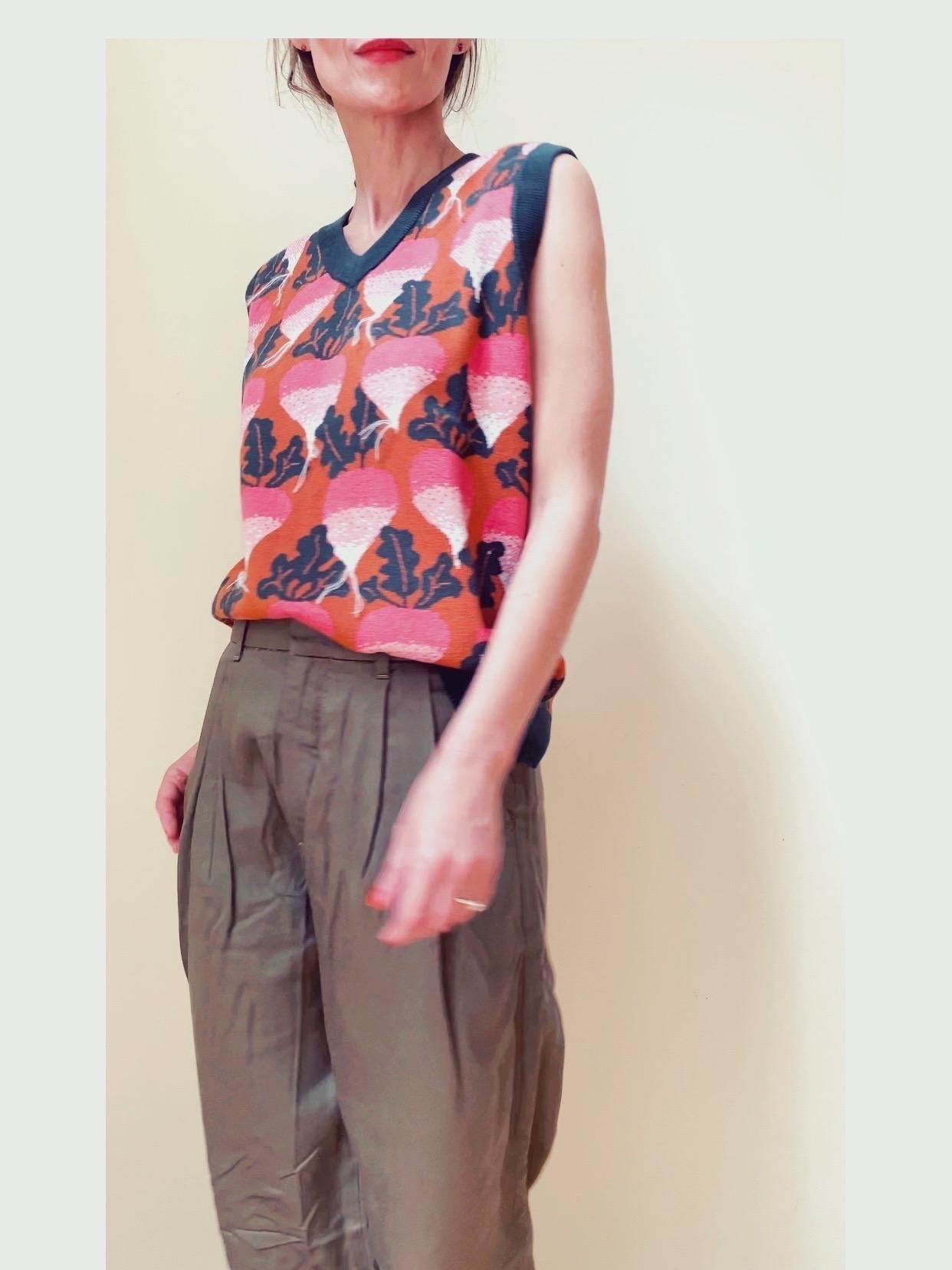 Person wearing a sleeveless top with a colorful leaf pattern and high-waisted pants on a plain background