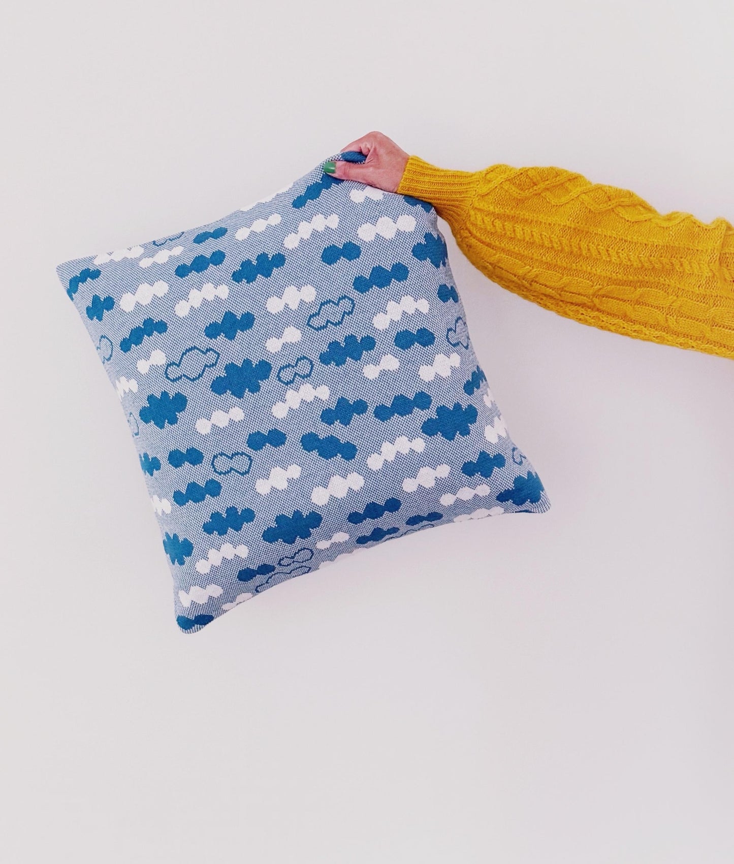 Blue pillow with cloud pattern held by a person wearing a yellow sweater on a white background