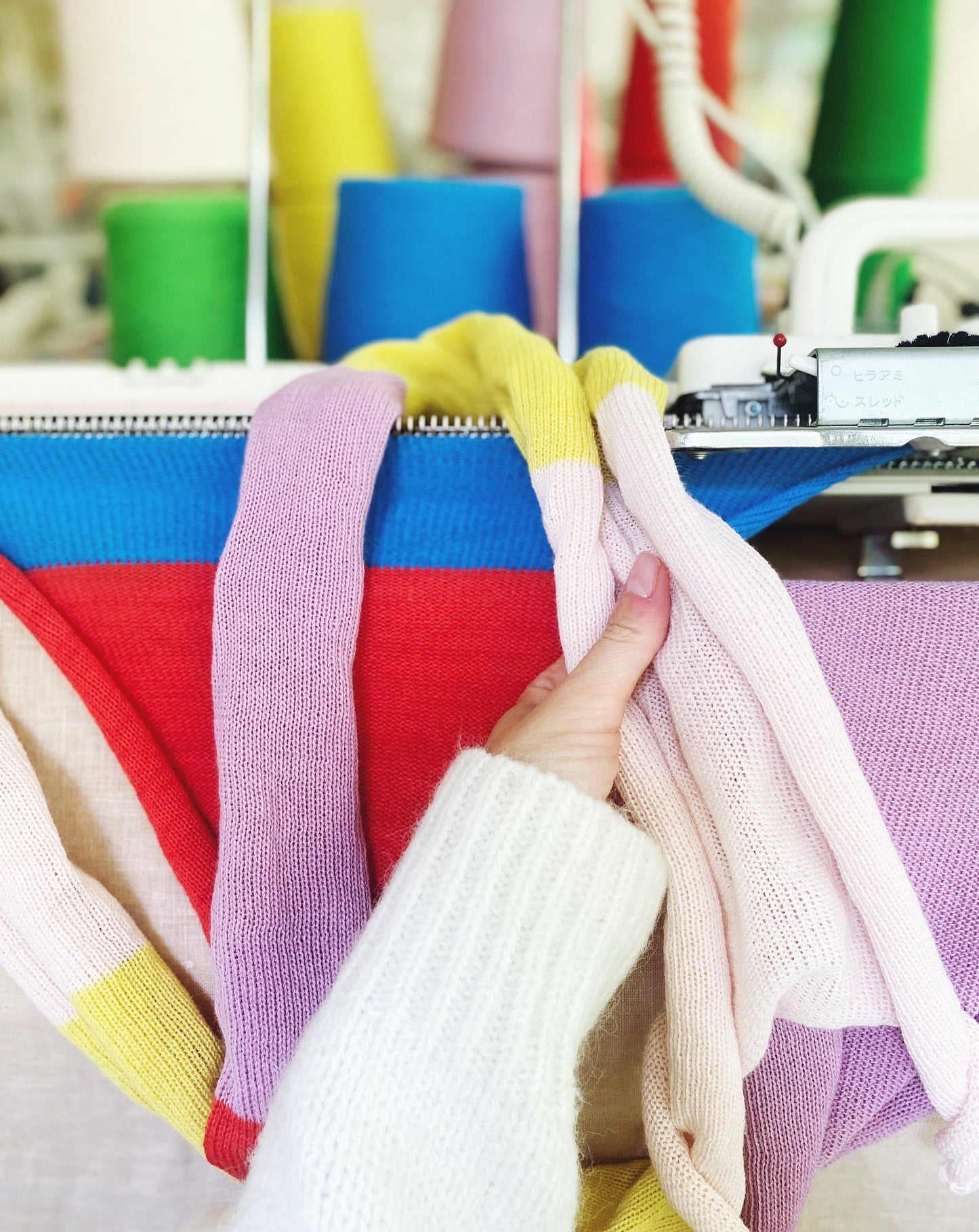 Colorful fabric swatches held by a hand with a knitting machine in the background