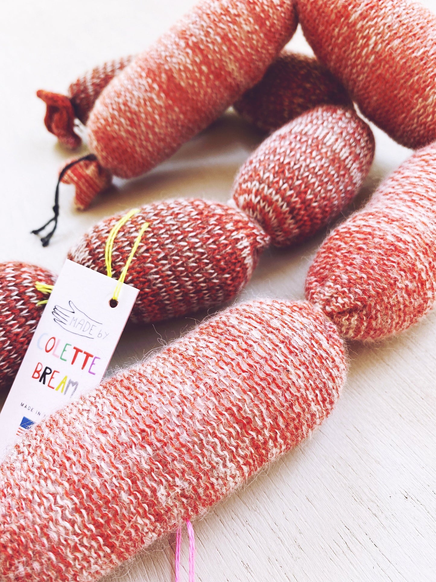 Lambswool knitted sausages on a light wooden surface with a visible brand tag.