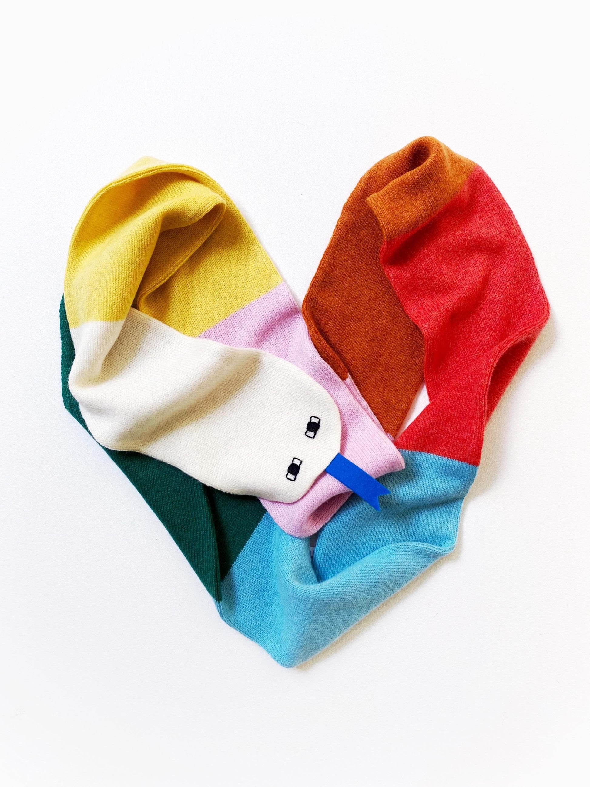 Colorful knitted lambswool scarf shaped like a snake arranged in a heart shape on a white background