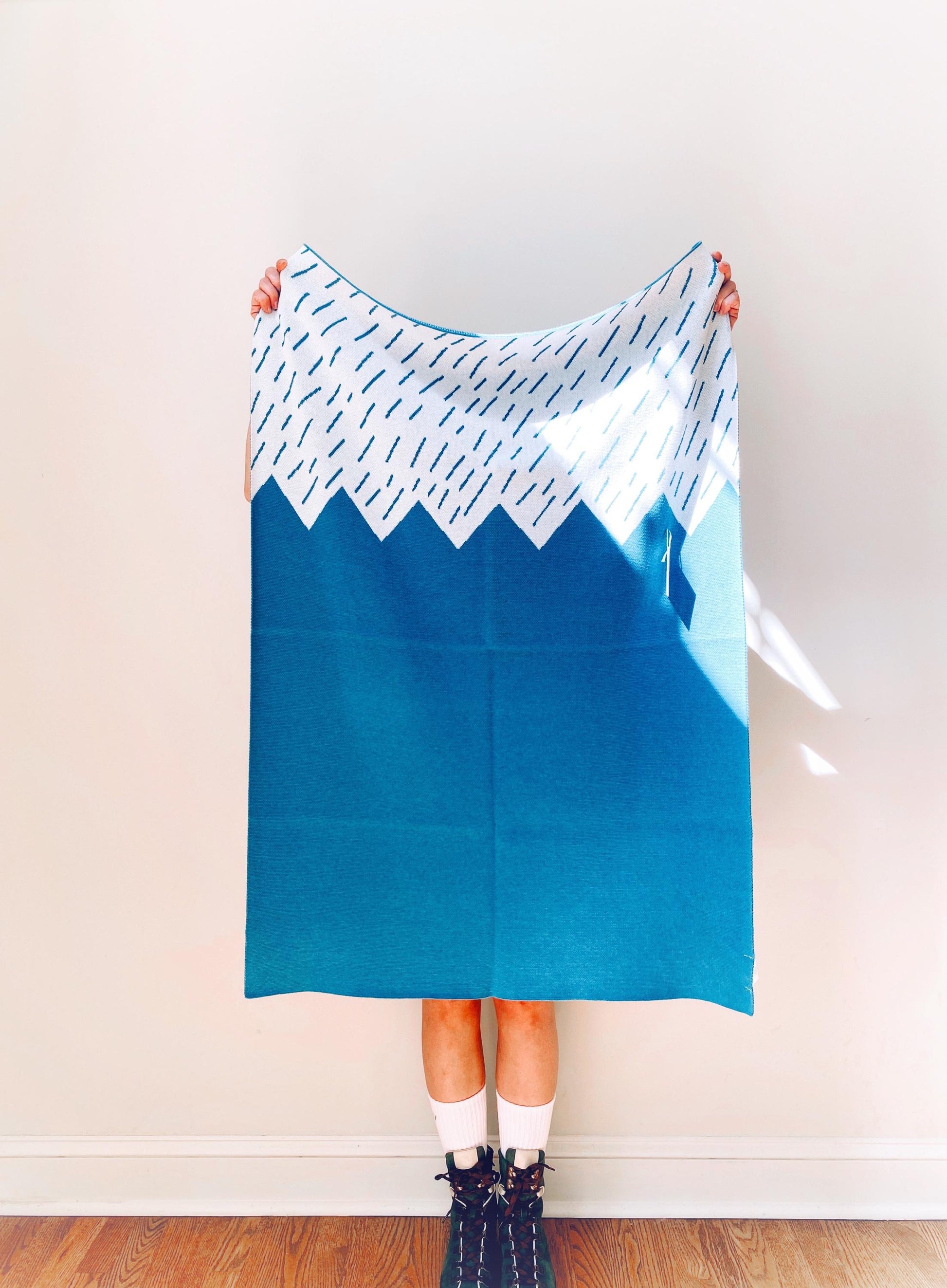 Person holding a blue knit blanket with mountain design against a plain background