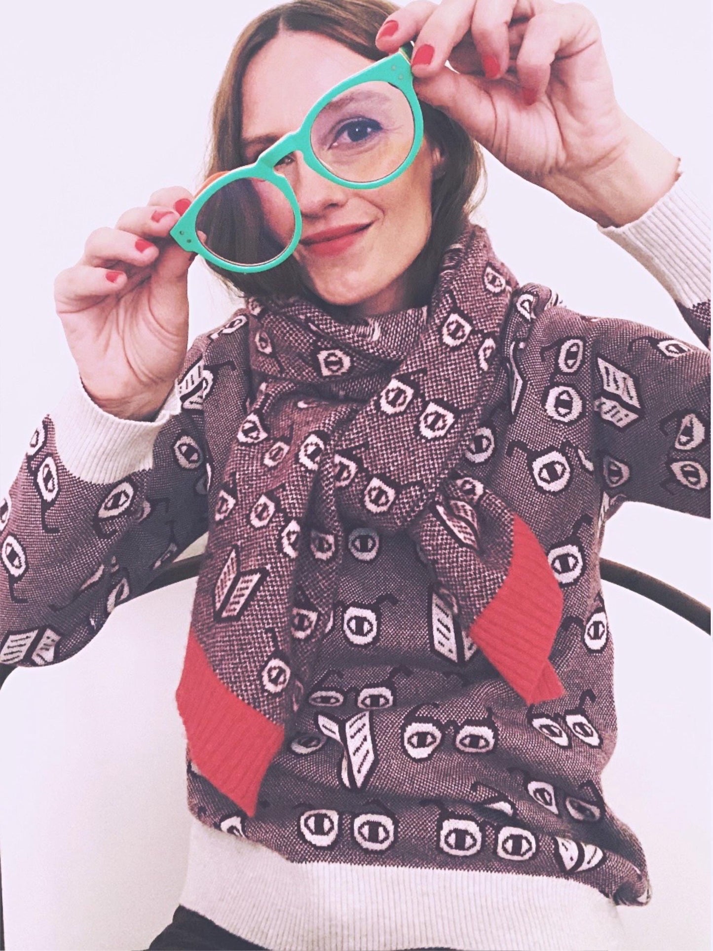 Person wearing a patterned spectacles eyeglasses sweater and scarf holding green eyeglasses