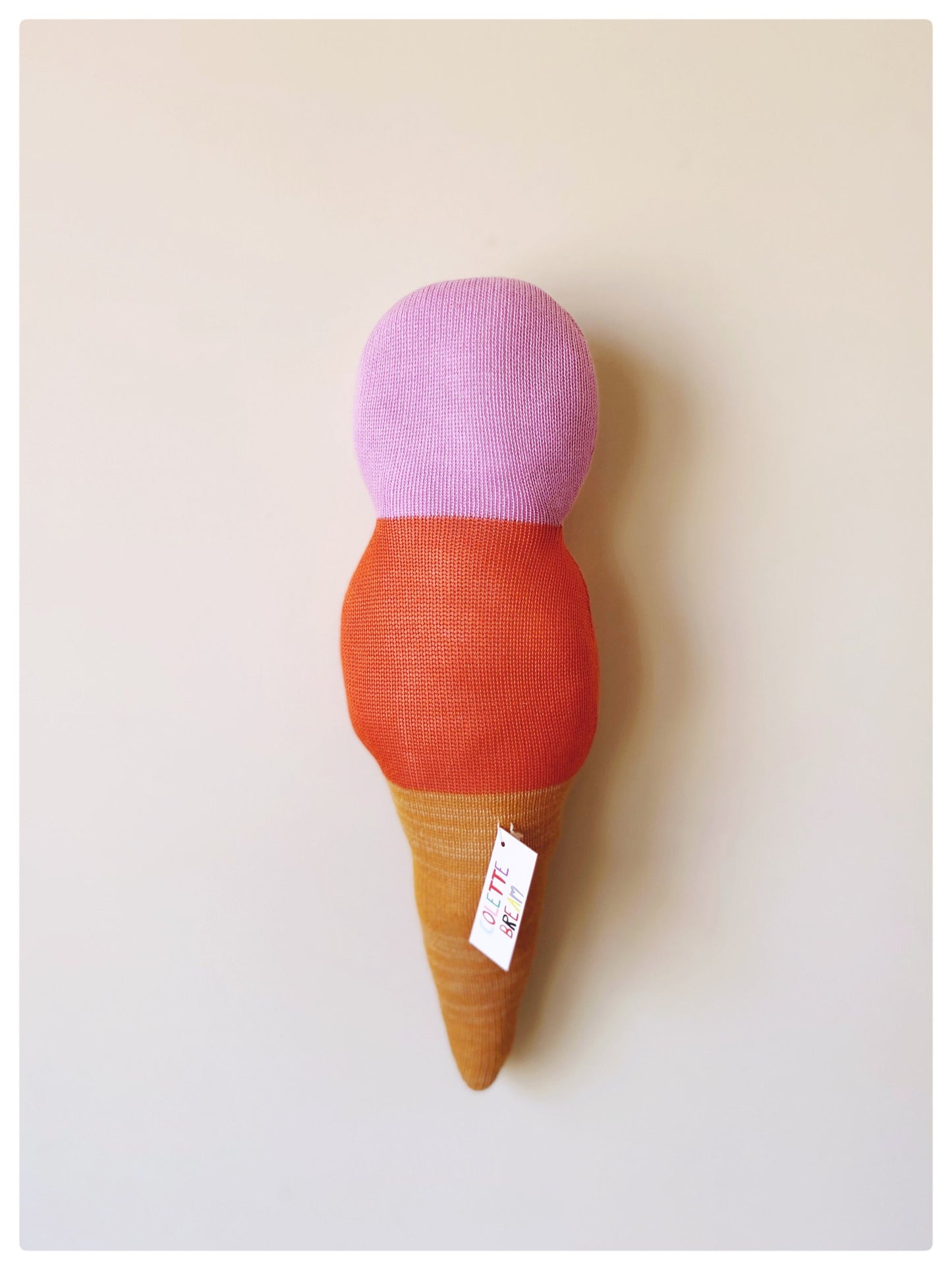Toy ice cream cone with pink top, orange middle, and brown base on a light background