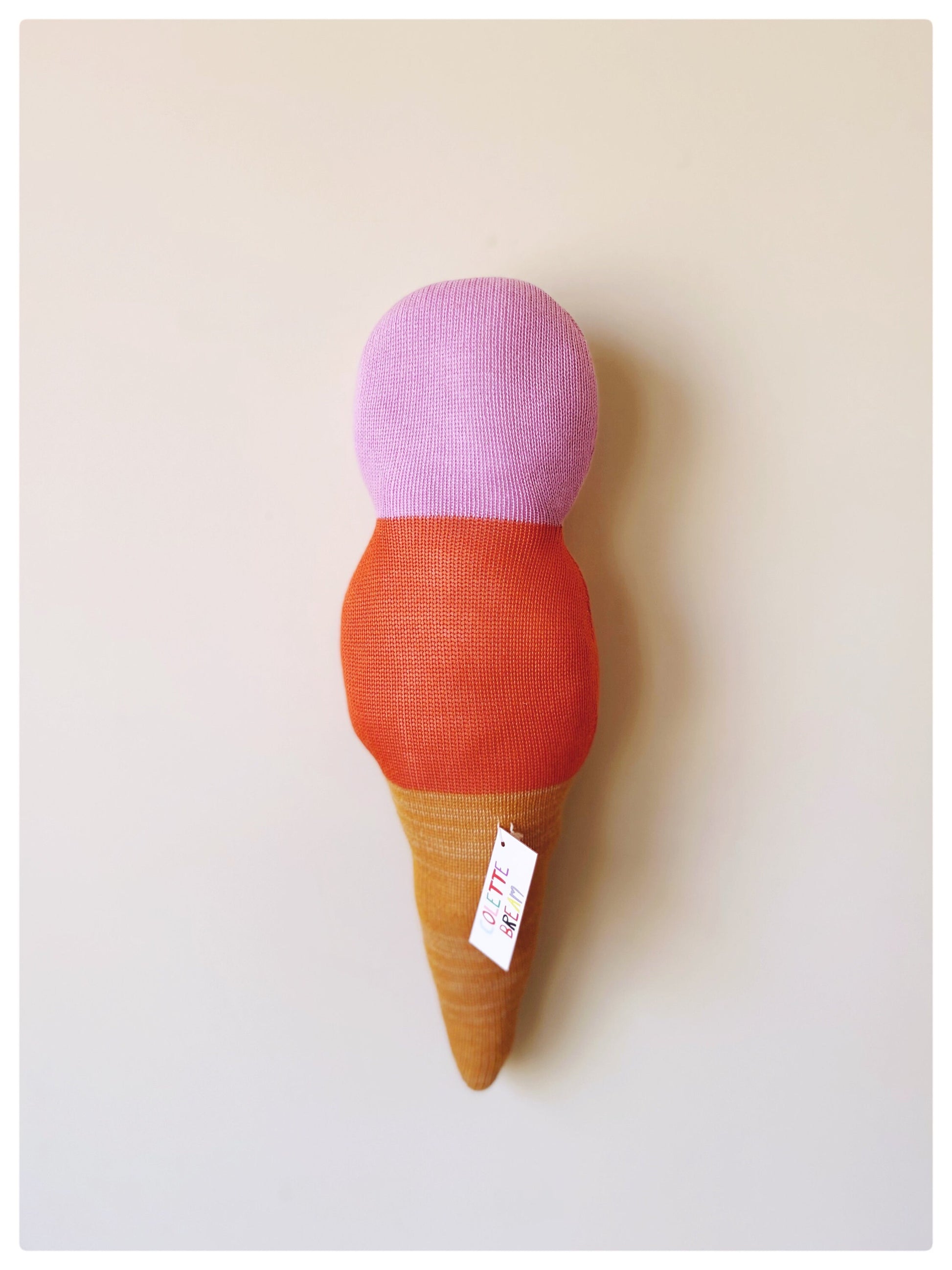 Toy ice cream cone with pink top, orange middle, and brown base on a light background