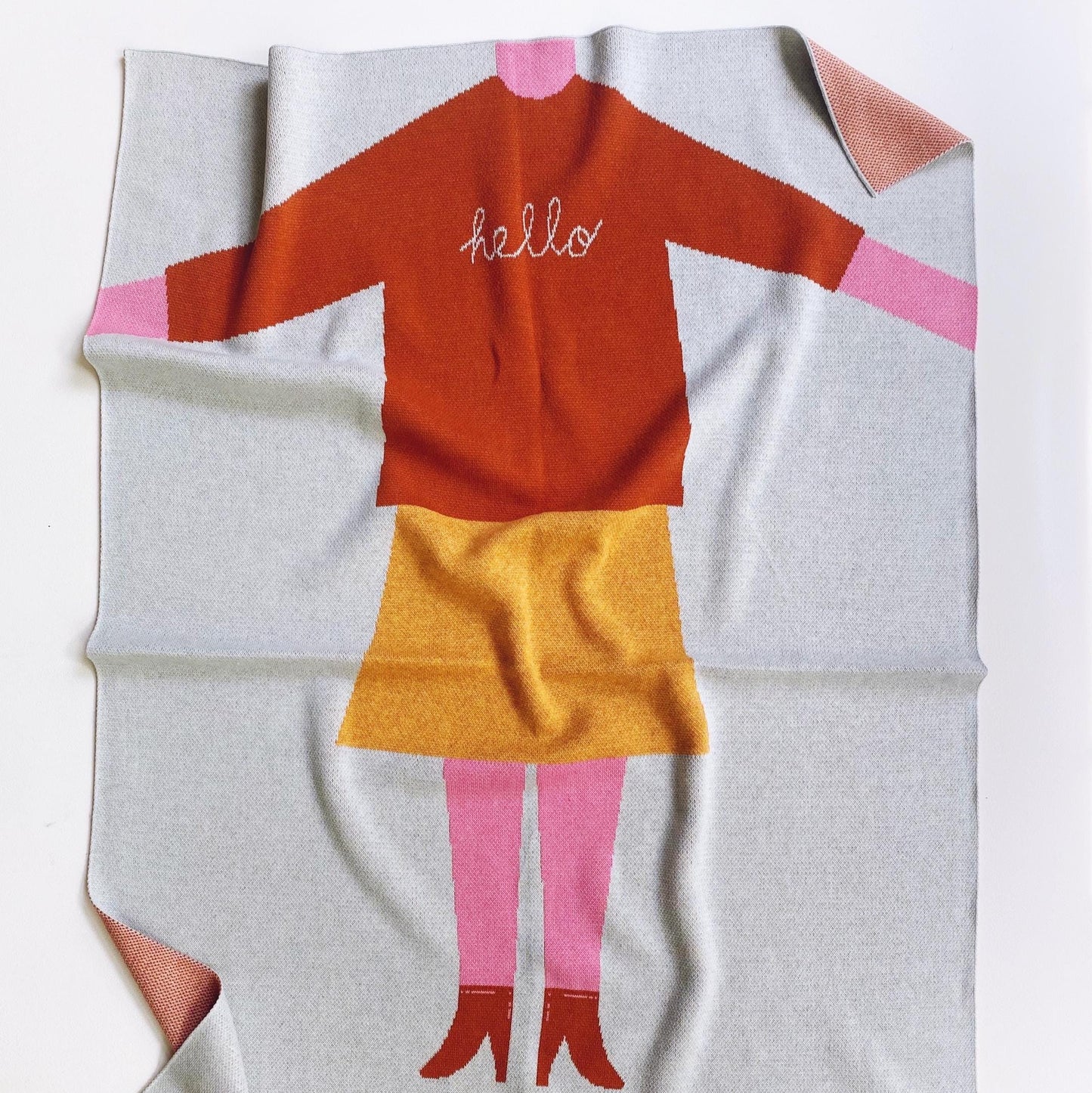 Knit baby blanket with a cartoon girl character wearing a red shirt and yellow skirt on a white background