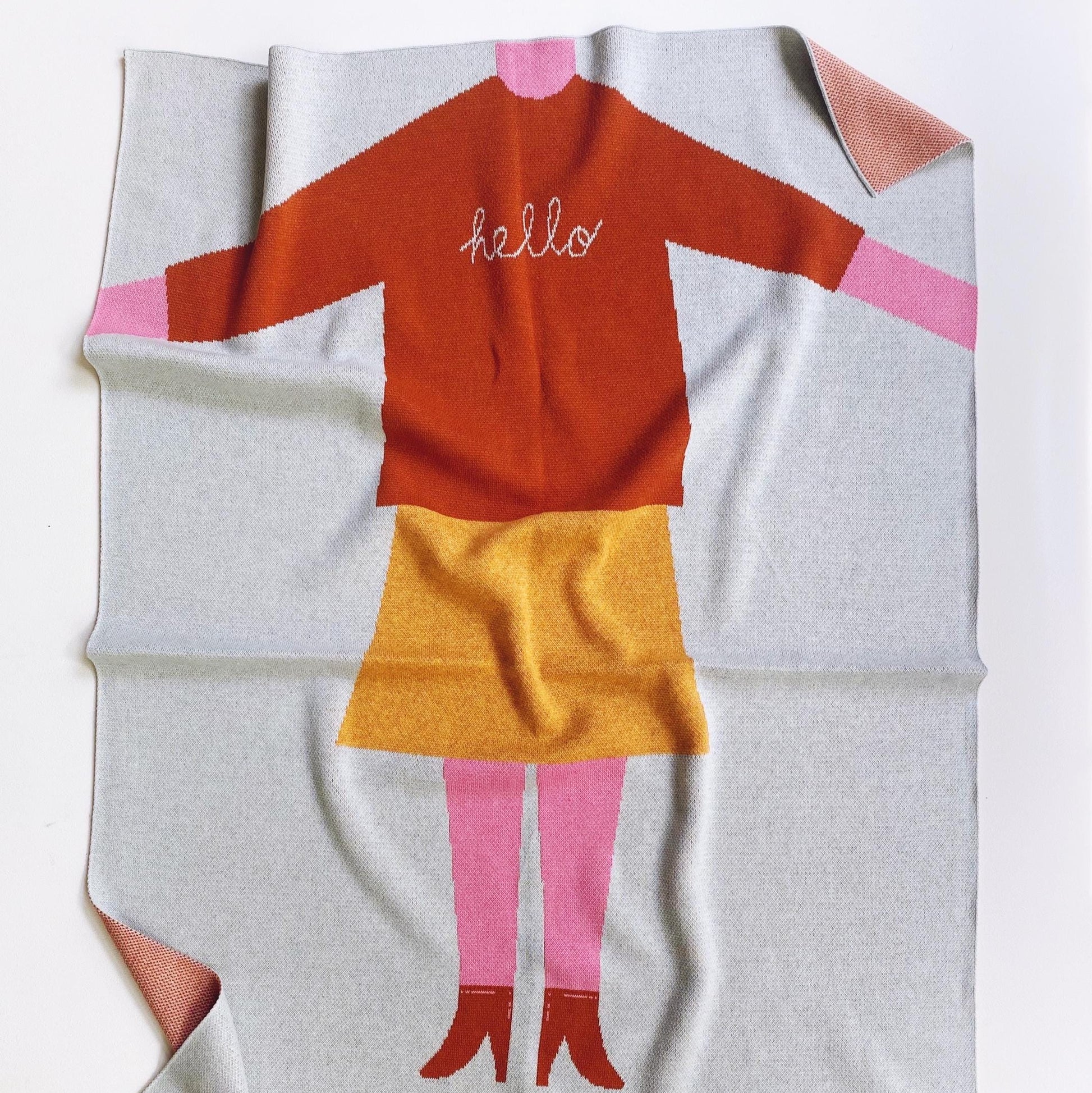 Knit baby blanket with a cartoon girl character wearing a red shirt and yellow skirt on a white background