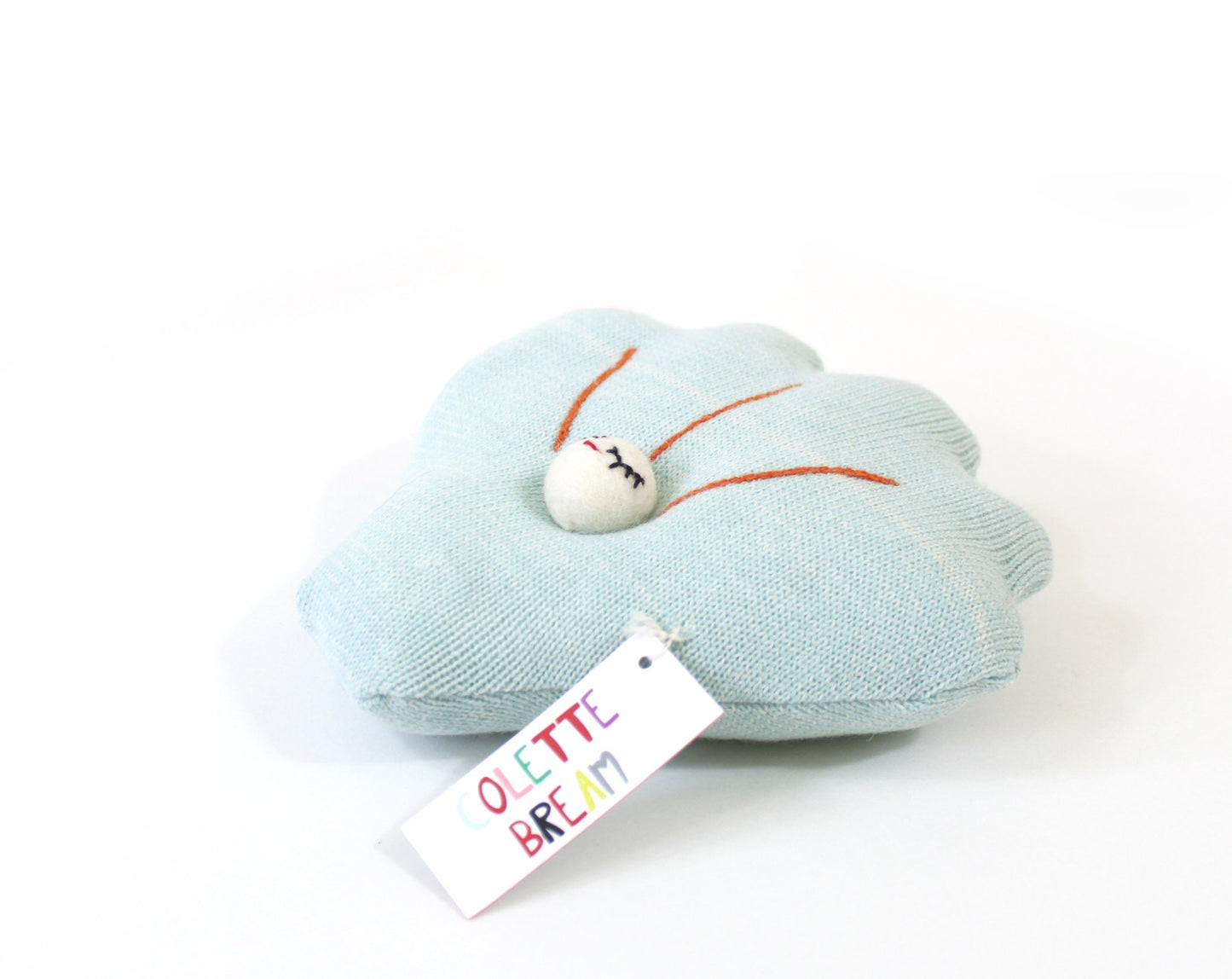 Light blue shell-shaped knitted pillow plush with a white tag on a white background