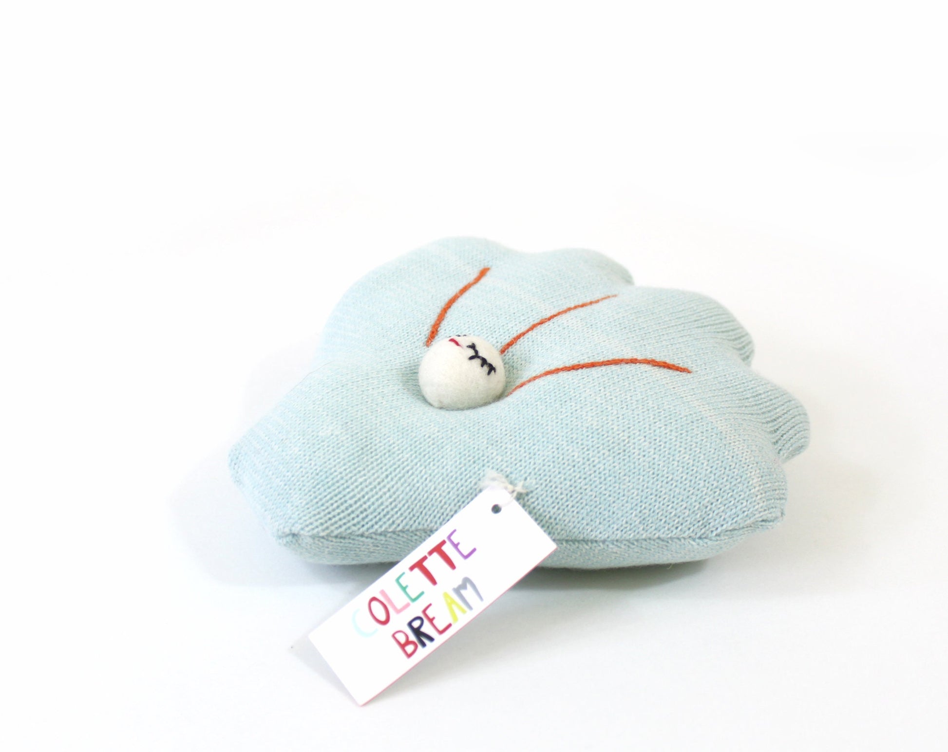 Light blue shell-shaped knitted pillow plush with a white tag on a white background