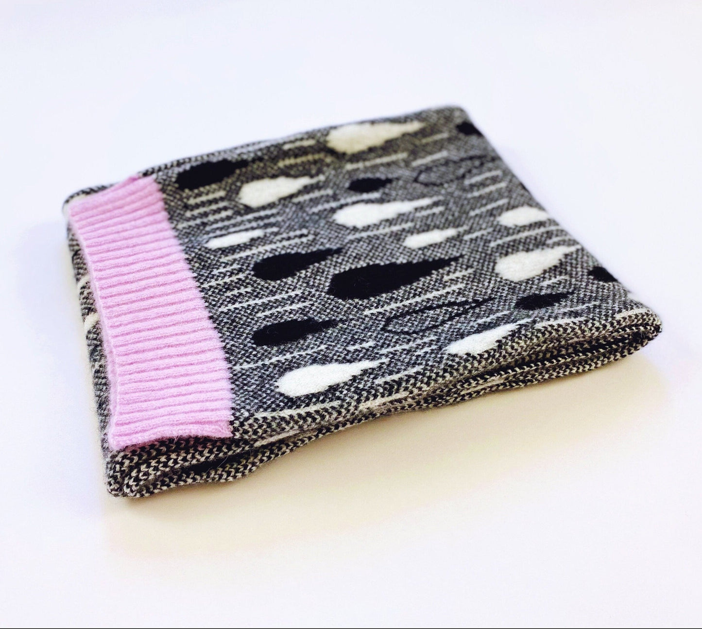 Textured knitted scarf with black and white raindrop pattern with a pink trim against a white background