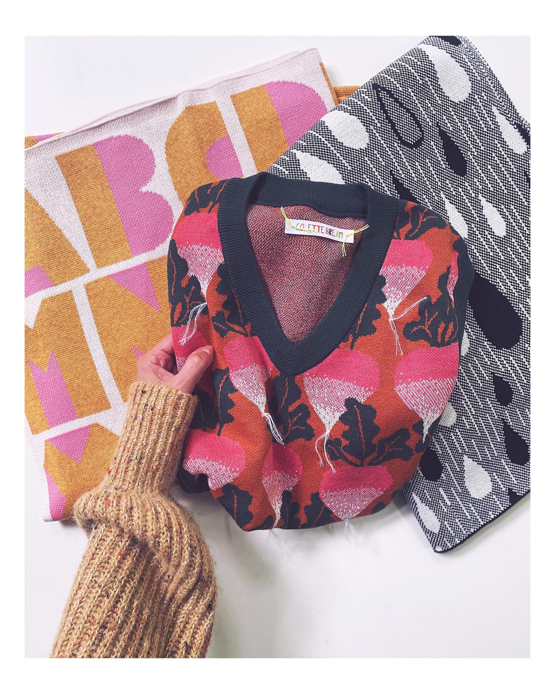 Person holding a collection of patterned knitted fabrics with colorful design on a white background