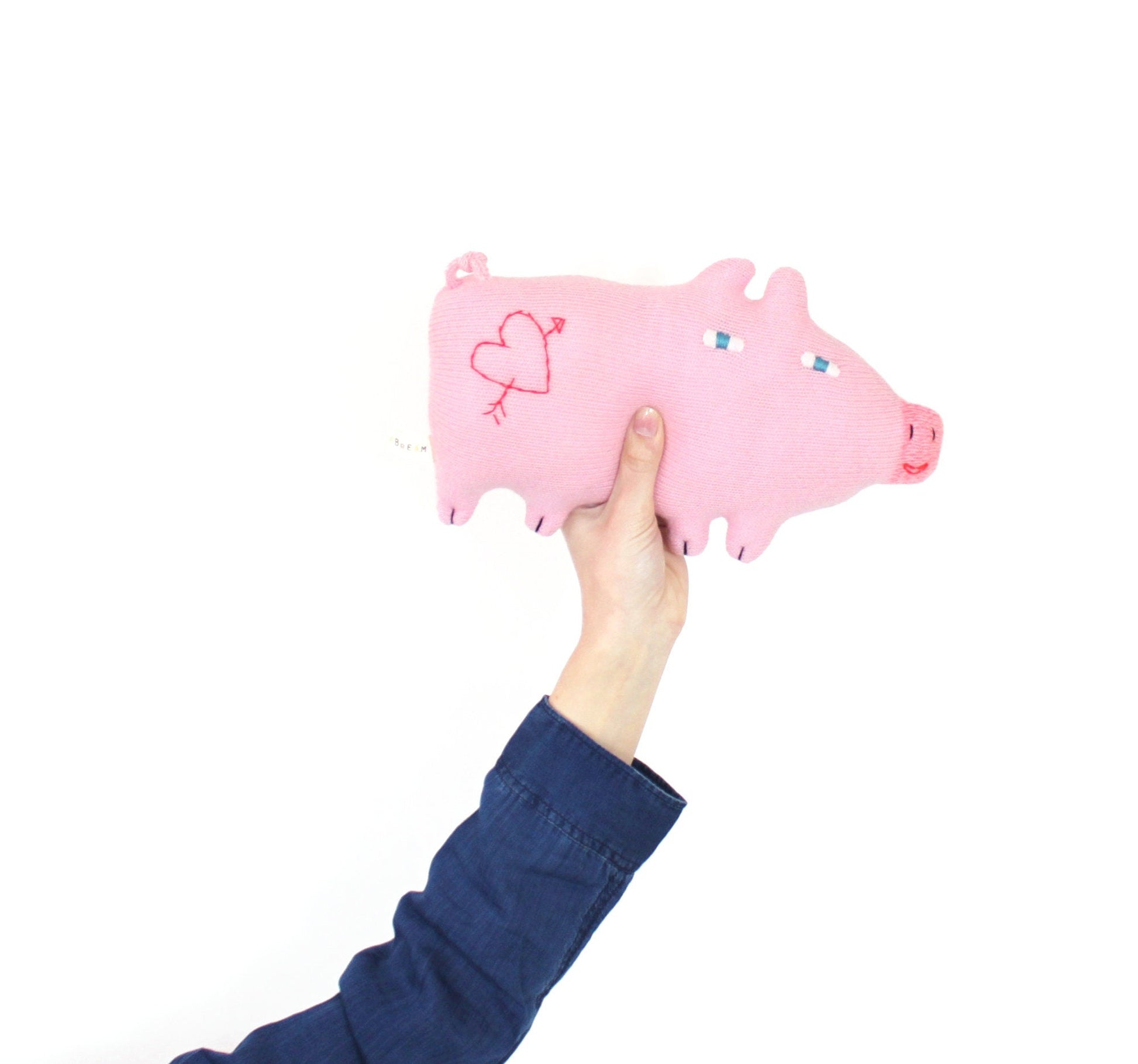 Pink knitted plush pig toy held by a hand on a white background