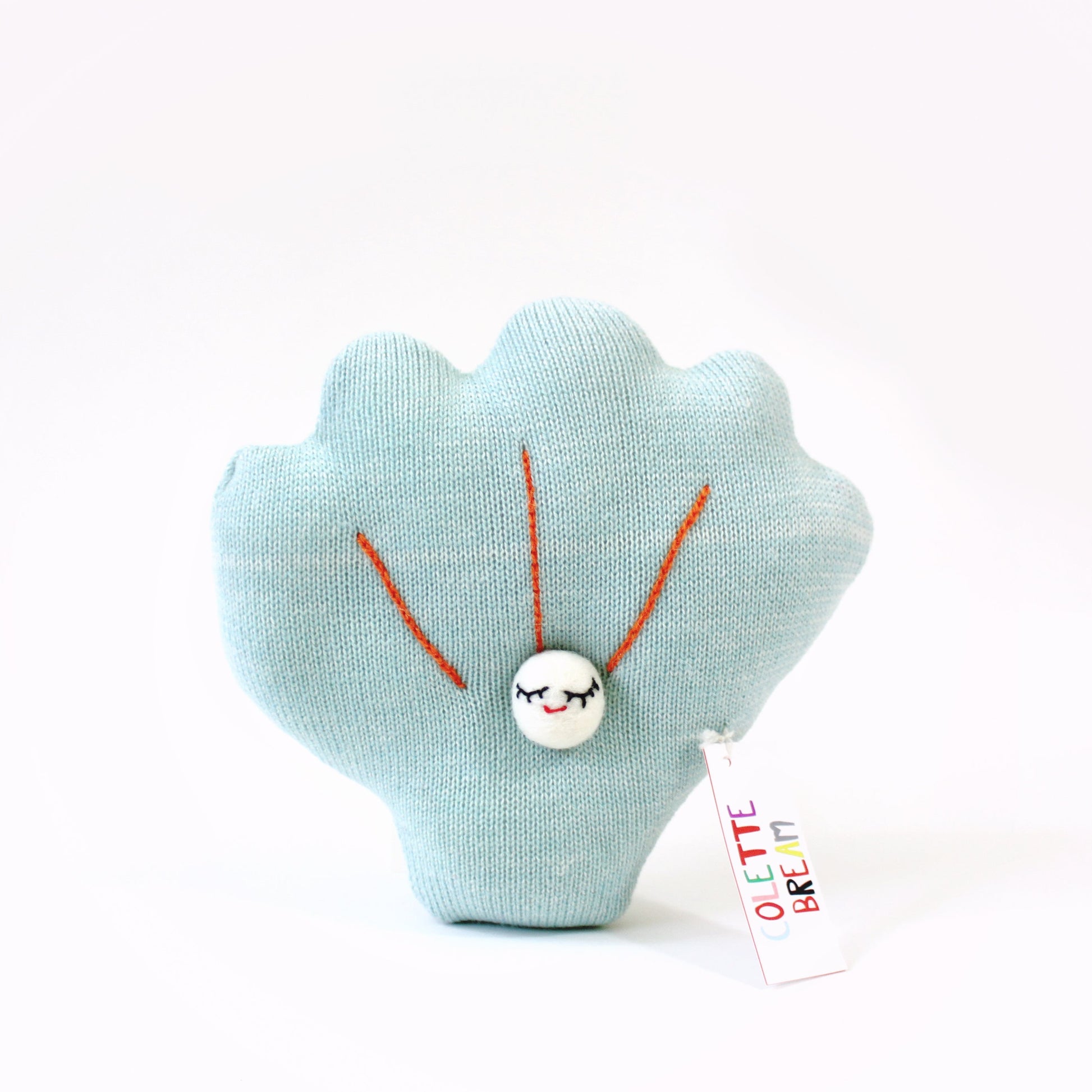 Light blue shell-shaped knitted plush toy with a white tag on a white background